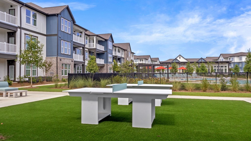 A white table sits in the middle of a grassy area in front of apartment buildings.