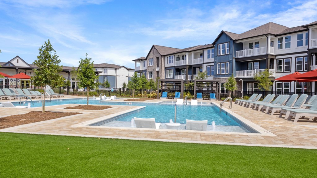 A large swimming pool surrounded by lawn chairs and trees in front of apartment buildings.