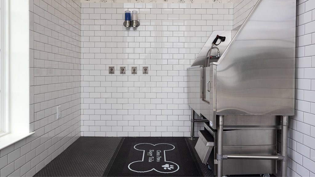 A clean, white tiled bathroom with a black mat on the floor.