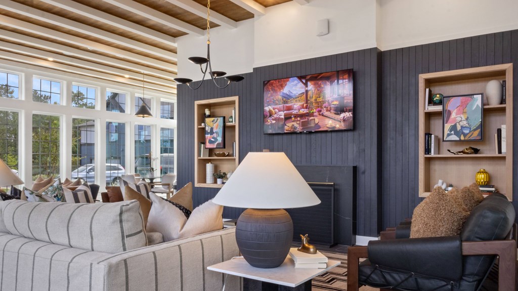 A living room with a grey couch, a black chair, a lamp, and a painting on the wall.