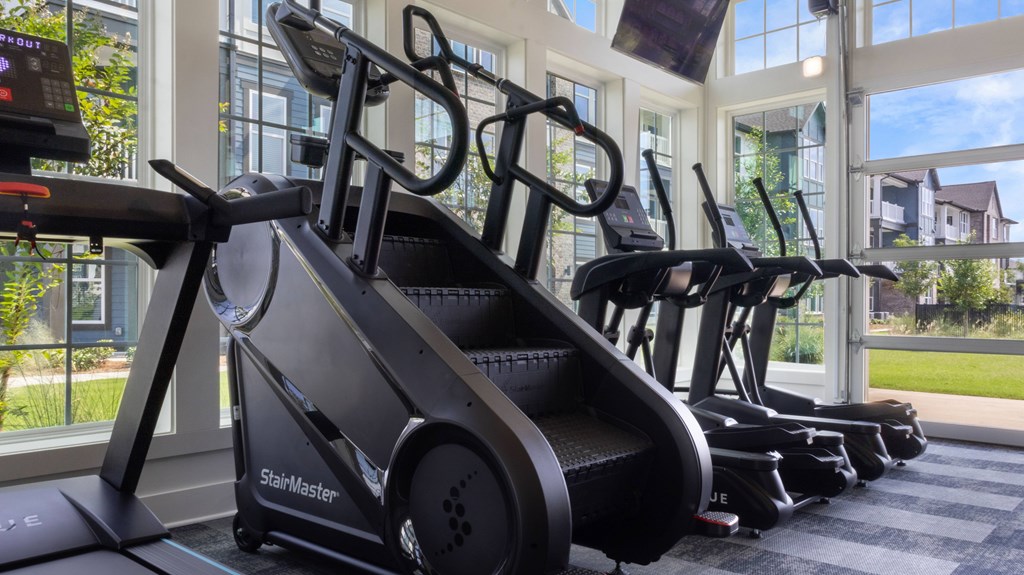 A StairMaster treadmill is in a row of treadmills in a gym with a view of the outside.