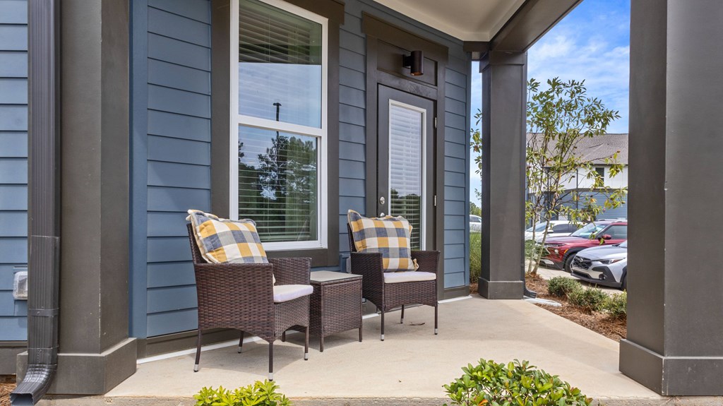 Two chairs and a table are on a porch.