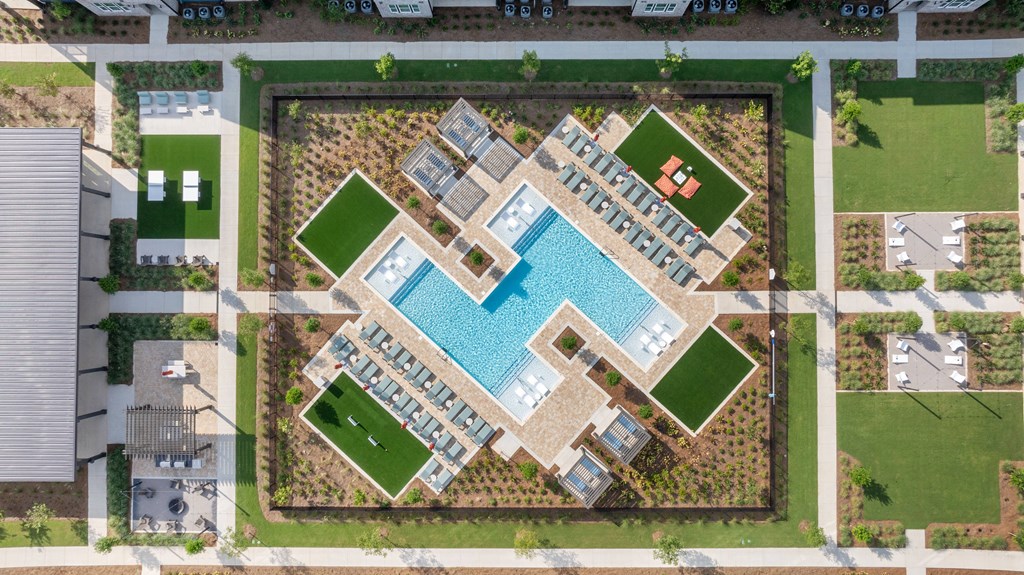 A large rectangular pool surrounded by a green lawn and a building.