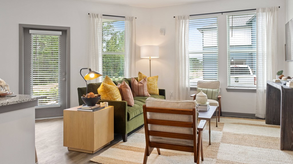 A living room with a green couch, a wooden chair, and a table with a lamp on it.