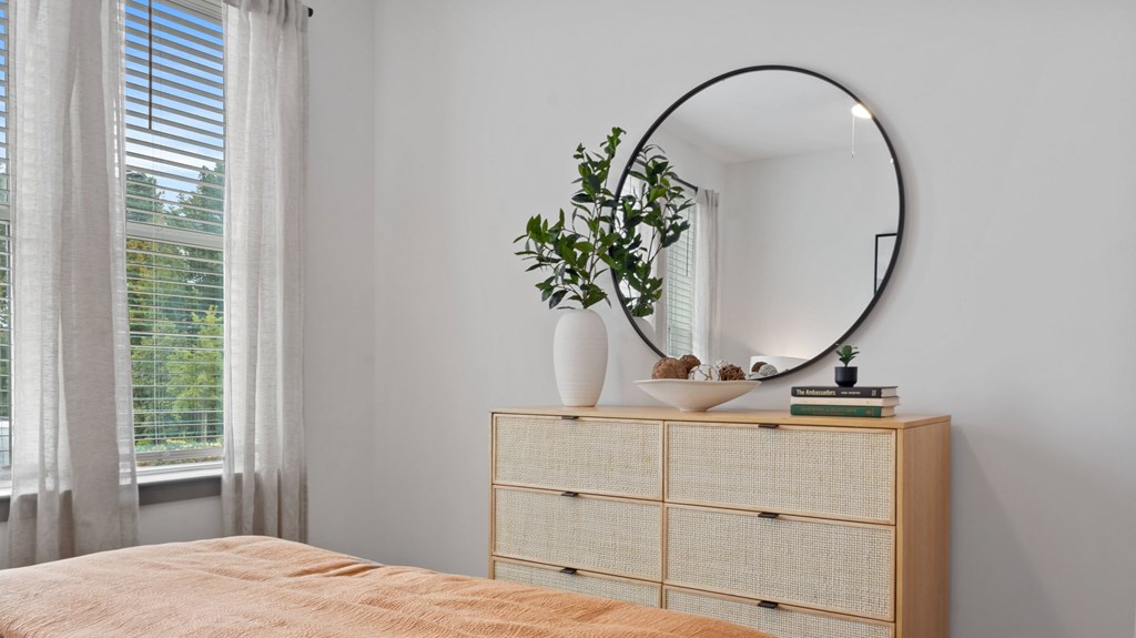 A round mirror sits on top of a wooden cabinet next to a vase with a plant.