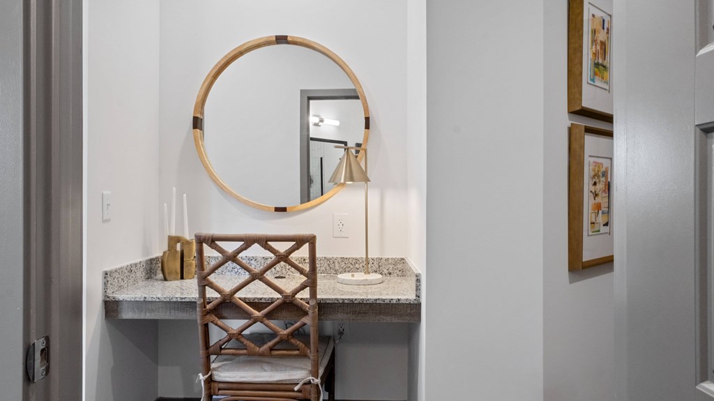 A wooden chair sits in front of a marble table with a round mirror above it.
