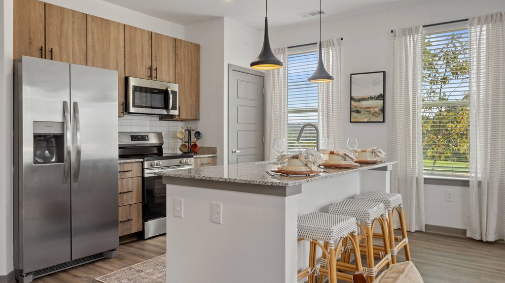 A kitchen with a refrigerator, microwave, and a dining table with chairs.