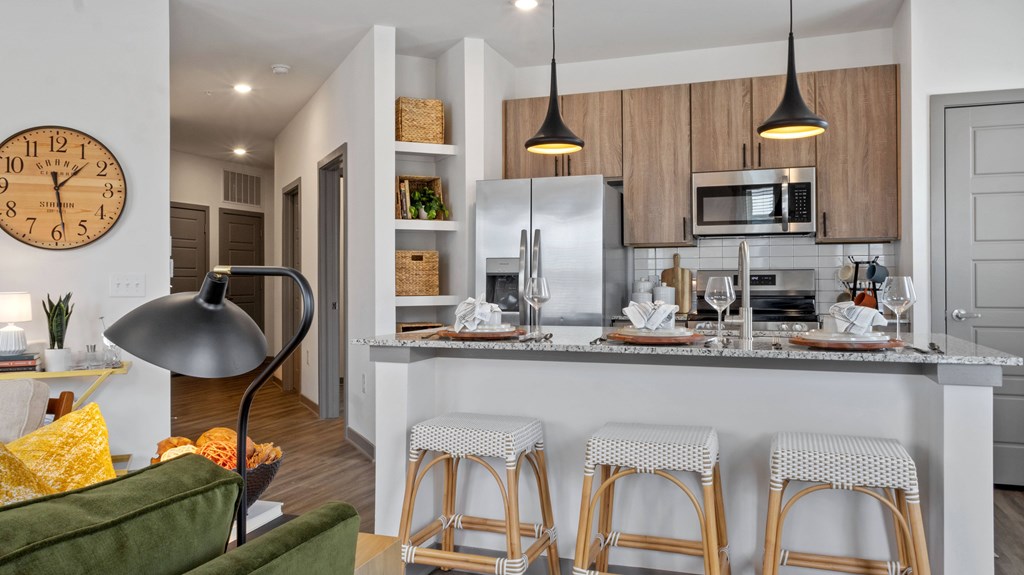 A kitchen with a clock on the wall and a bar area with stools.