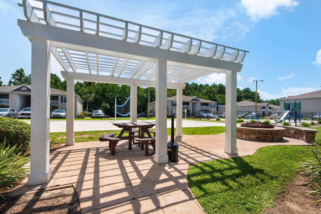A white pergola with a picnic table underneath it and a fire place to the side at Crystal Lake in Pensacola, Florida.