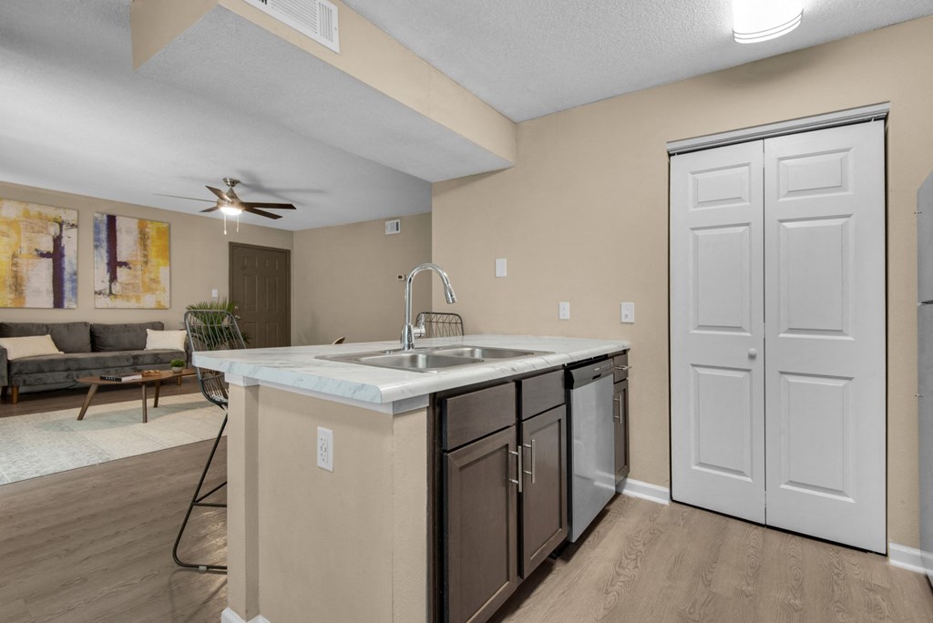 A stainless-steel kitchen sink surrounded by granite countertop, dishwasher, and white wood pantry at Crystal Lake in Pensacola, Florida.