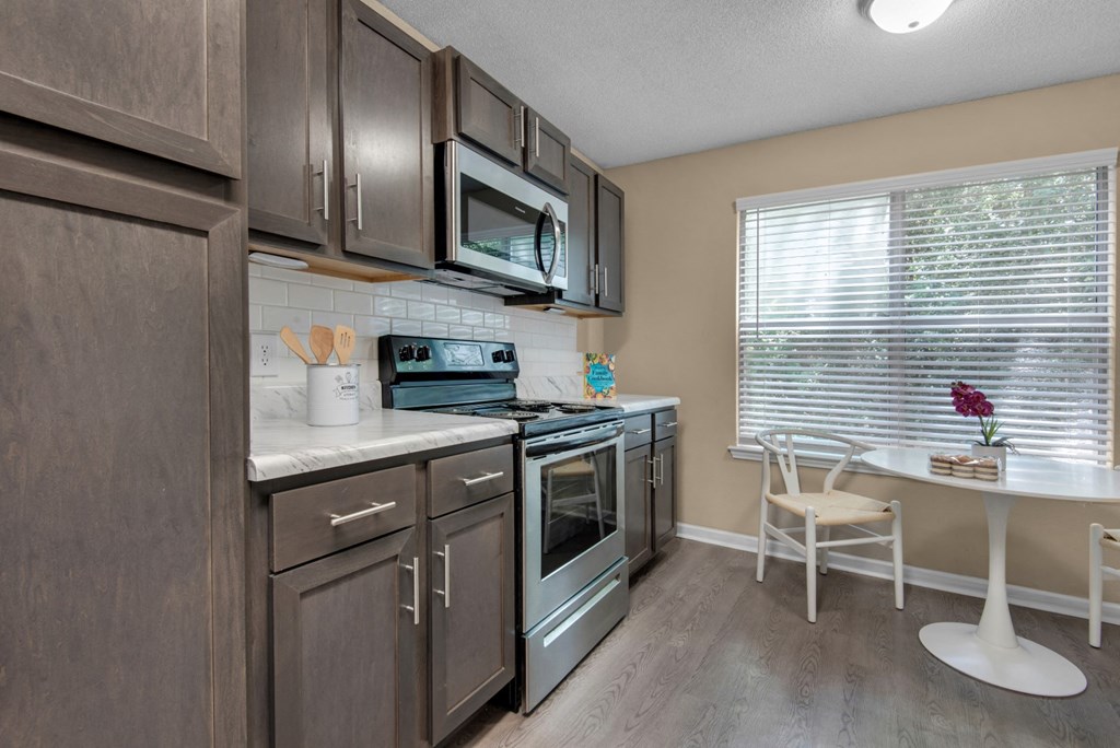 A kitchen with brown cabinets, stainless-steel appliances, granite countertops, and a white tile backsplash at Crystal Lake in Pensacola, Florida.
