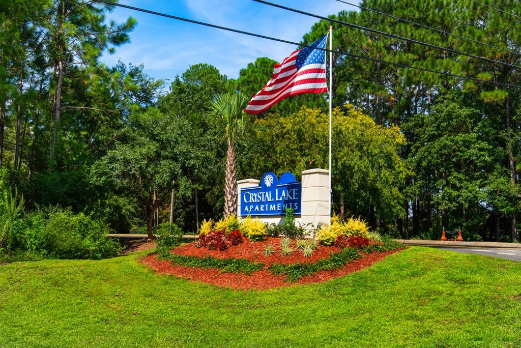 A sign for Crystal Lake Apartments is in front of  beautiful landscape in Pensacola, Florida.