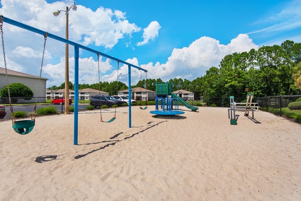 A playground with swings, a slide, and a seesaw at Crystal Lake Apartments in Pensacola, FL.
