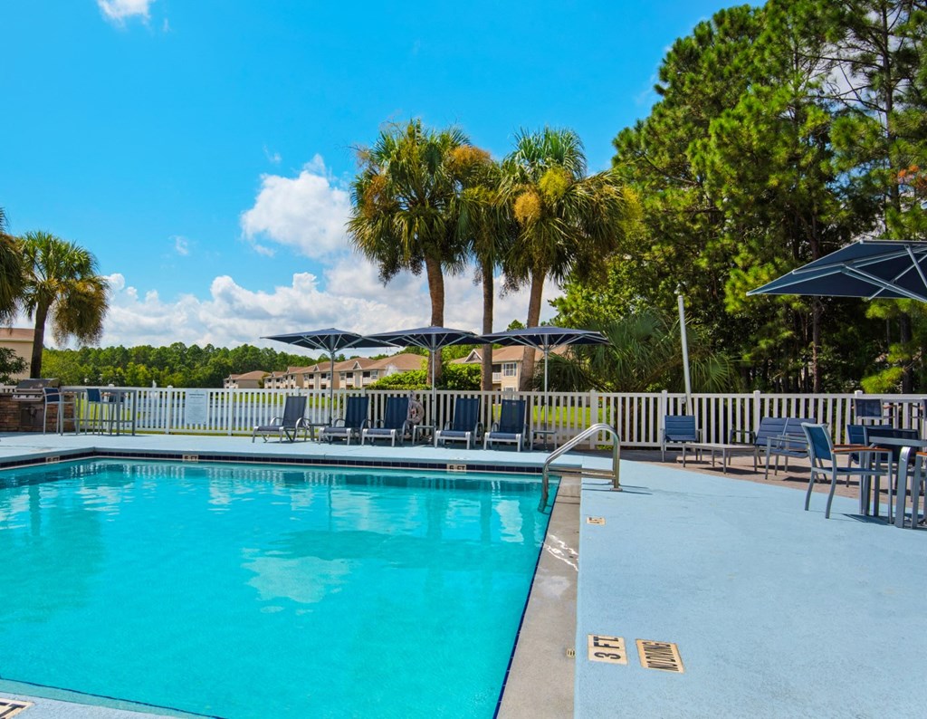 A large, gated, swimming pool with ladder access surrounded by palm trees and lounge chairs at Crystal Lake in Pensacola, Florida.
