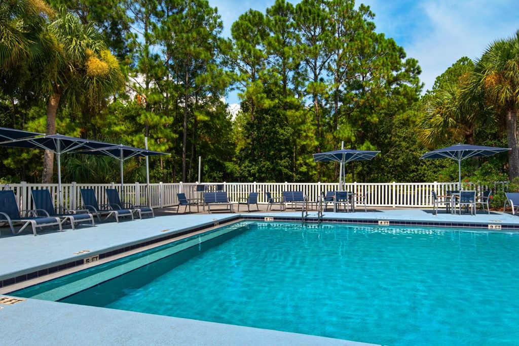An outdoor swimming pool surrounded by lounge chairs and umbrellas at Crystal Lake in Pensacola, Florida.