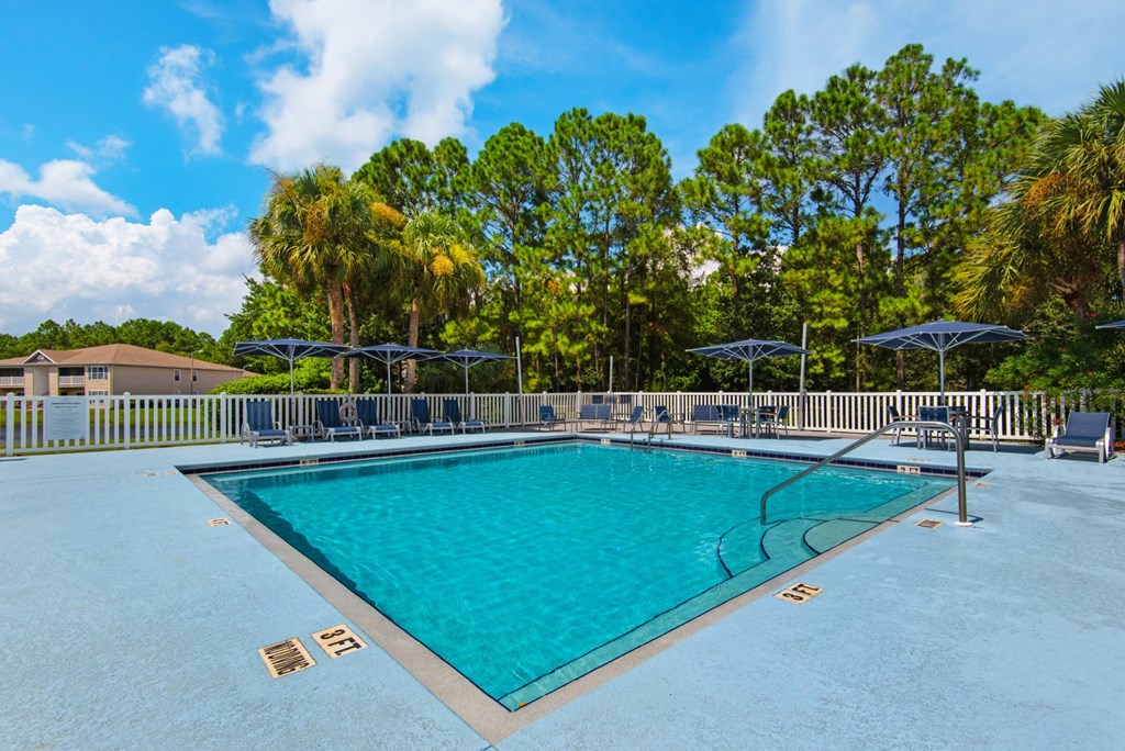 An outdoor swimming pool surrounded by trees and umbrellas at Crystal Lake in Pensacola, Florida.