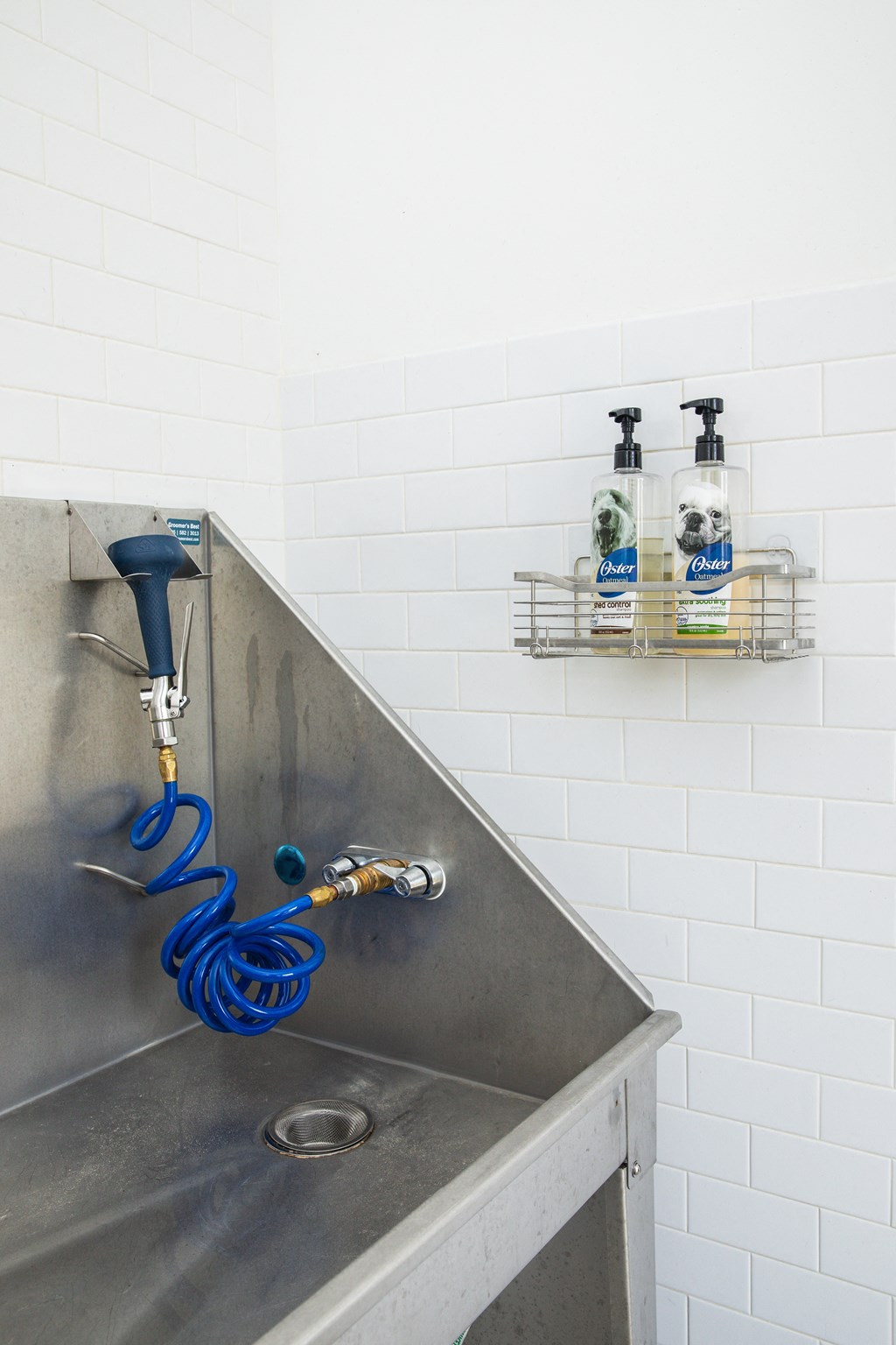 a stainless steel sink in a bathroom with white tiles and a soap dispenser on