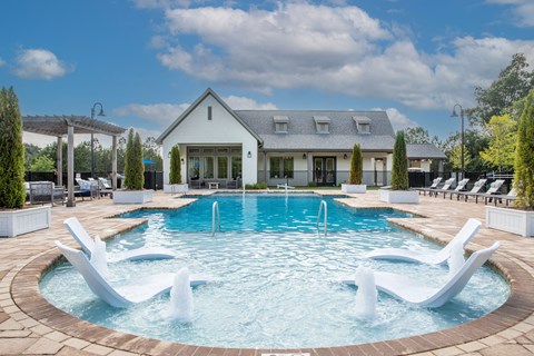 a large pool with white chairs and a house in the background