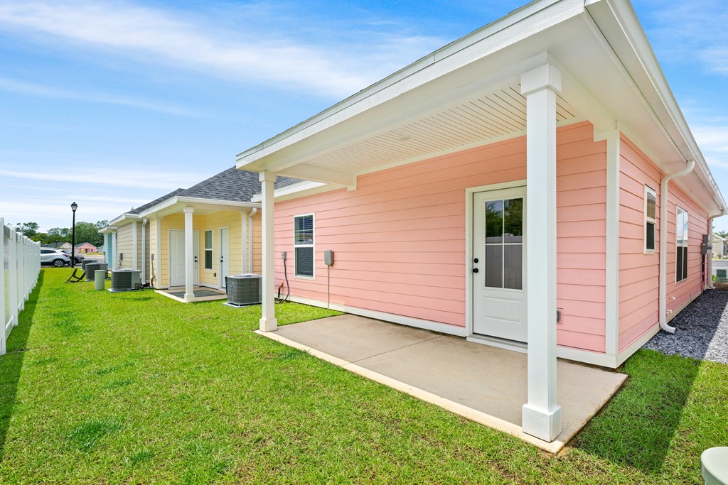 the front of a pink house with a porch and grass