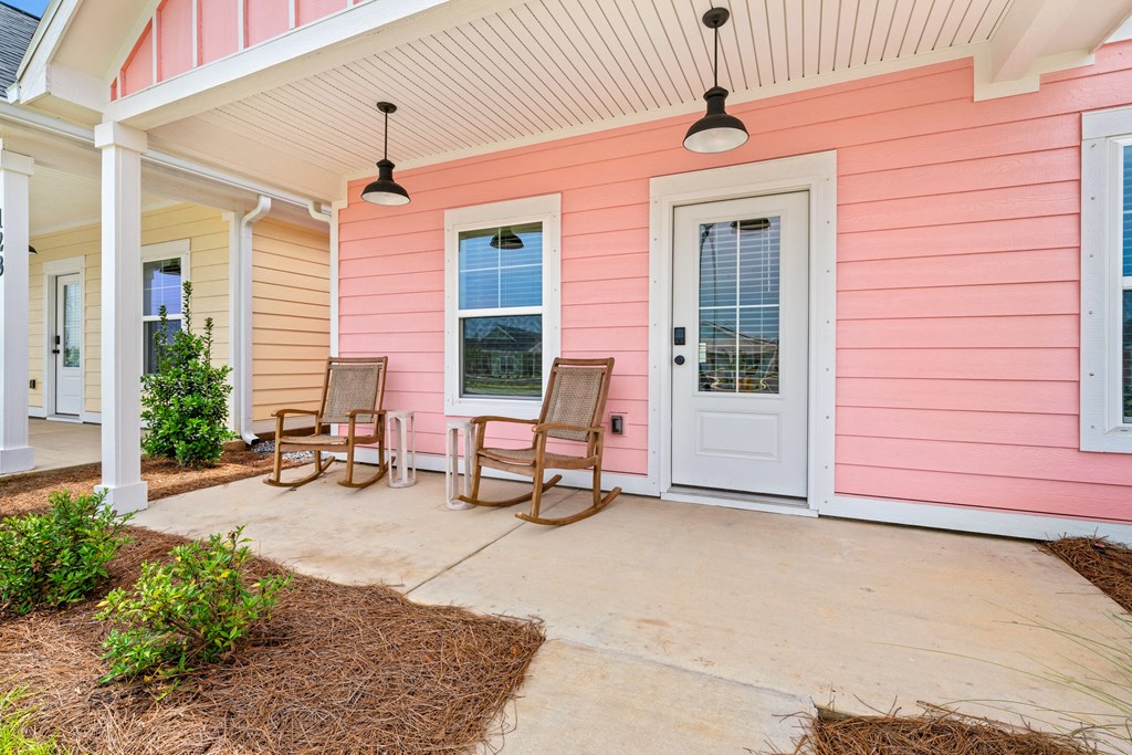 the front porch of a pink house with two rocking chairs