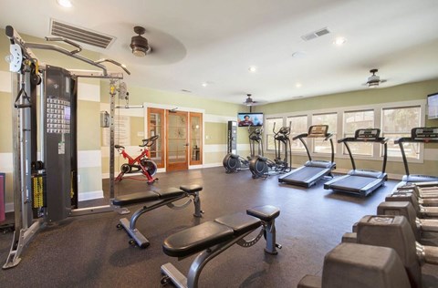 a gym with weights and cardio equipment and a tv