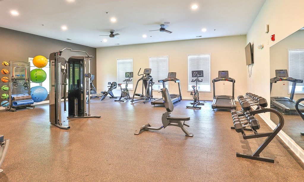 a gym with cardio equipment and weights in a building with windows