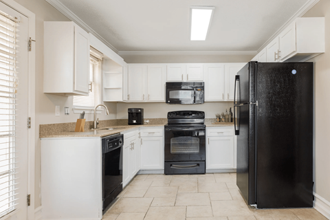 A black refrigerator stands in a kitchen with white cabinets and appliances.