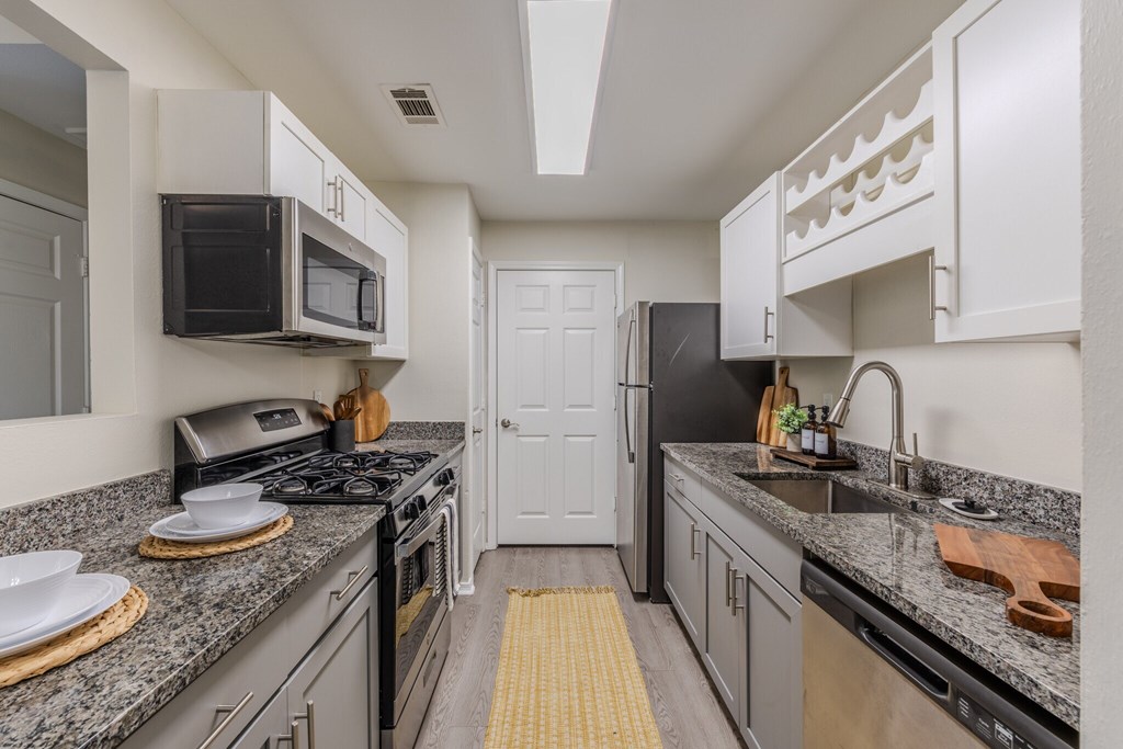 Kitchen with granite countertop and wood-designed flooring A kitchen with a black stove top oven and a black microwave above it at Grande View Apartments in Biloxi, MS