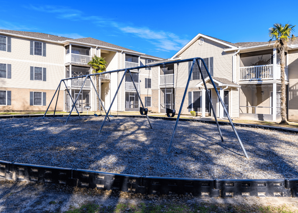 A playground with a swing set in front of apartment buildings  at Grande View Apartments in Biloxi, MS