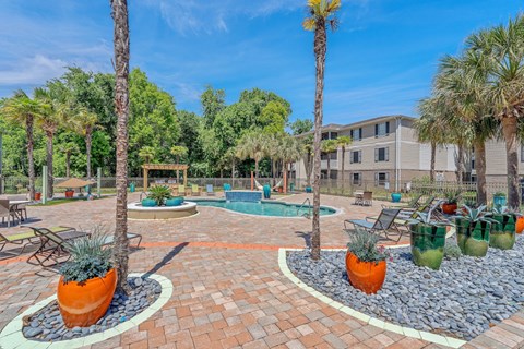 A sunny day at a poolside with a palm tree and a building in the background.