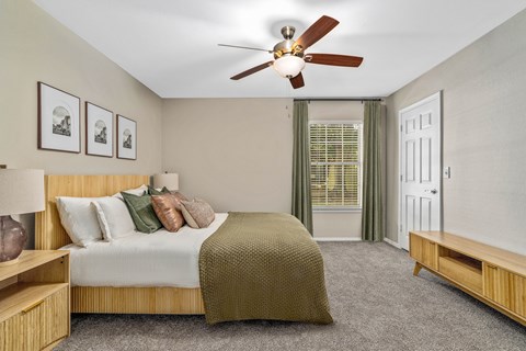 A bedroom with a bed, a ceiling fan, and a window with green curtains.