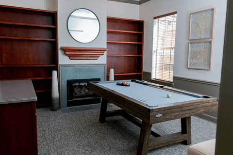 A pool table in a room with a fireplace and bookshelves.