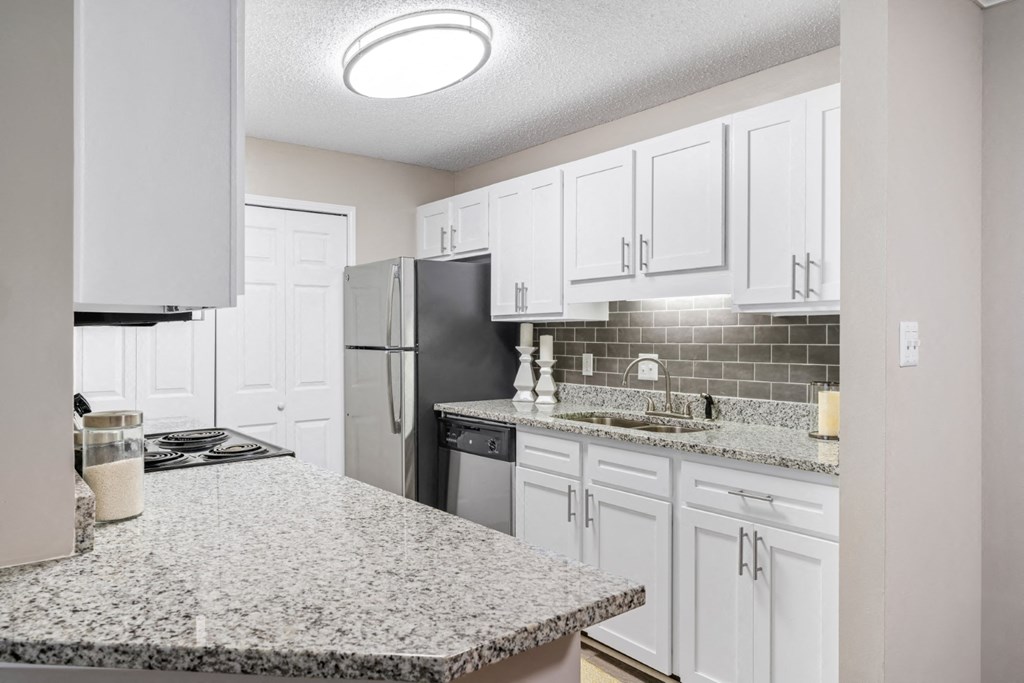 A kitchen with granite countertops, white cabinets, and a laundry closet at Summerchase at Riverchase in Hoover, Alabama.