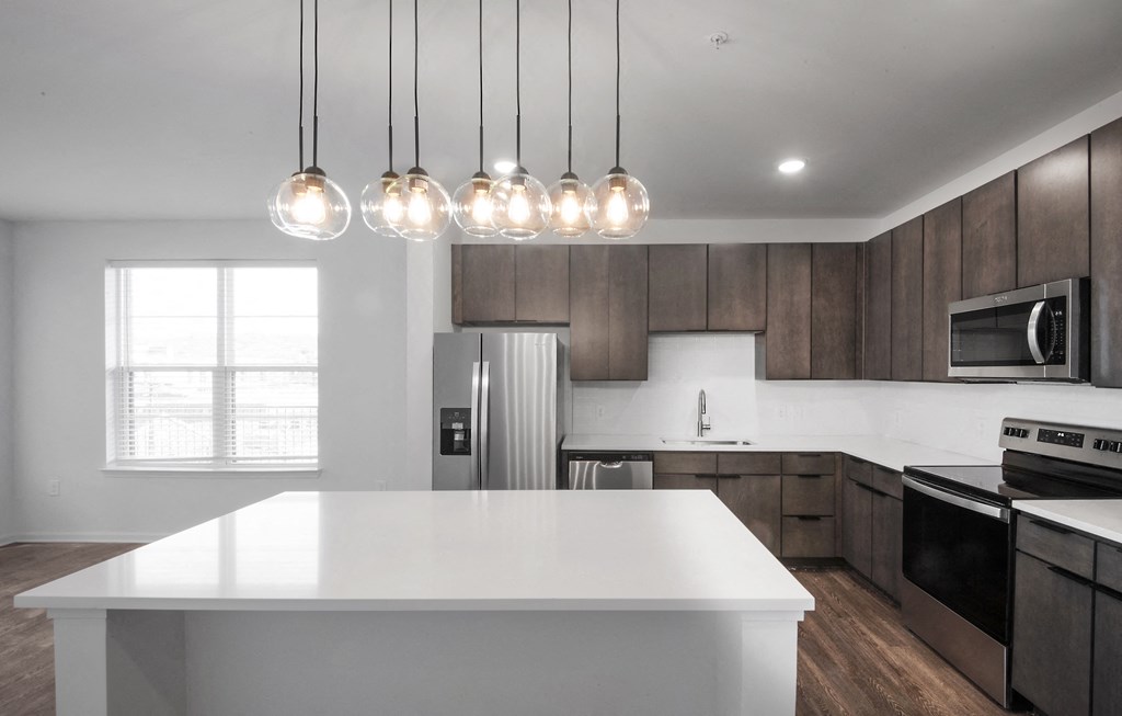 an open kitchen with a white counter top and a large island with lights at Artisan Flats in Birmingham, AL