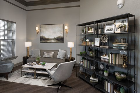 A living room with a grey sofa, a white chair, a coffee table, and a bookshelf with various decorative items.
