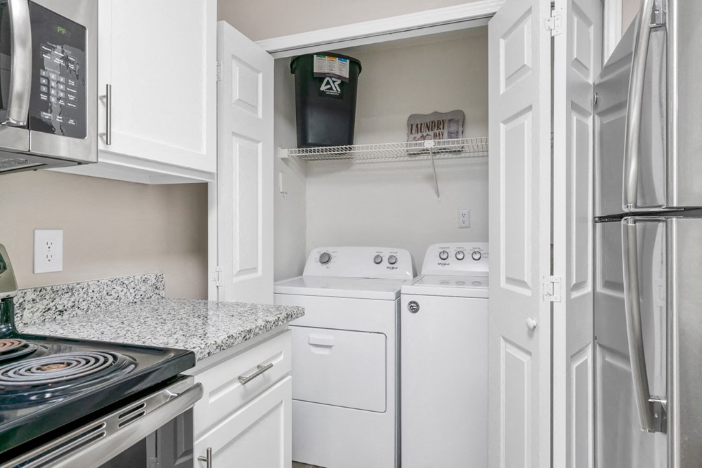A kitchen with granite countertops, white cabinets, and a washer and dryer unit at Summerchase at Riverchase in Hoover, Alabama.