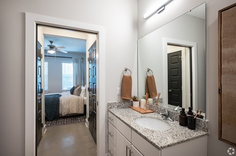 A bathroom with a large mirror and a bedroom visible through the door.