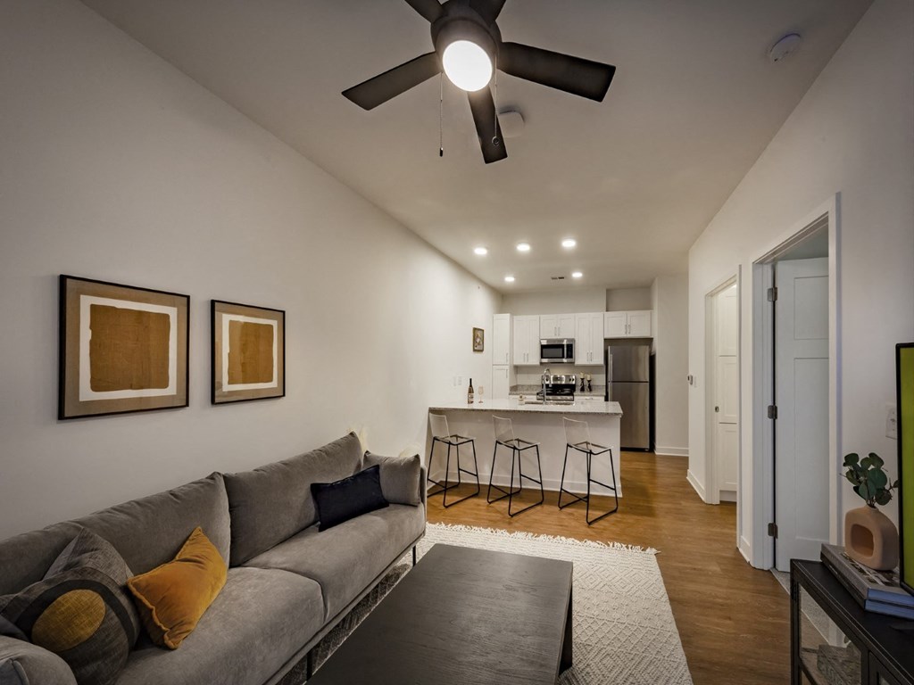 A living room with a ceiling fan and wood-look flooring that opens to the kitchen at Wesley Place Apartments in Indianapolis, IN.