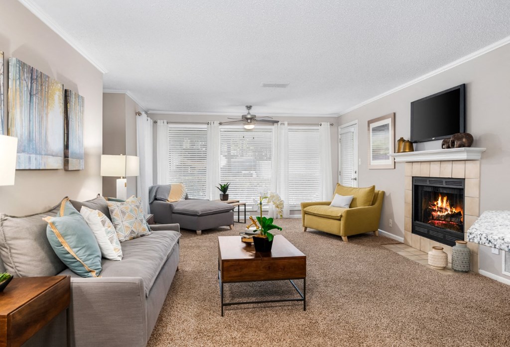 A carpeted living room with a tiel-surround fireplace, floor-to-ceiling windows, and a ceiling fan at Summerchase at Riverchase in Hoover, Alabama.