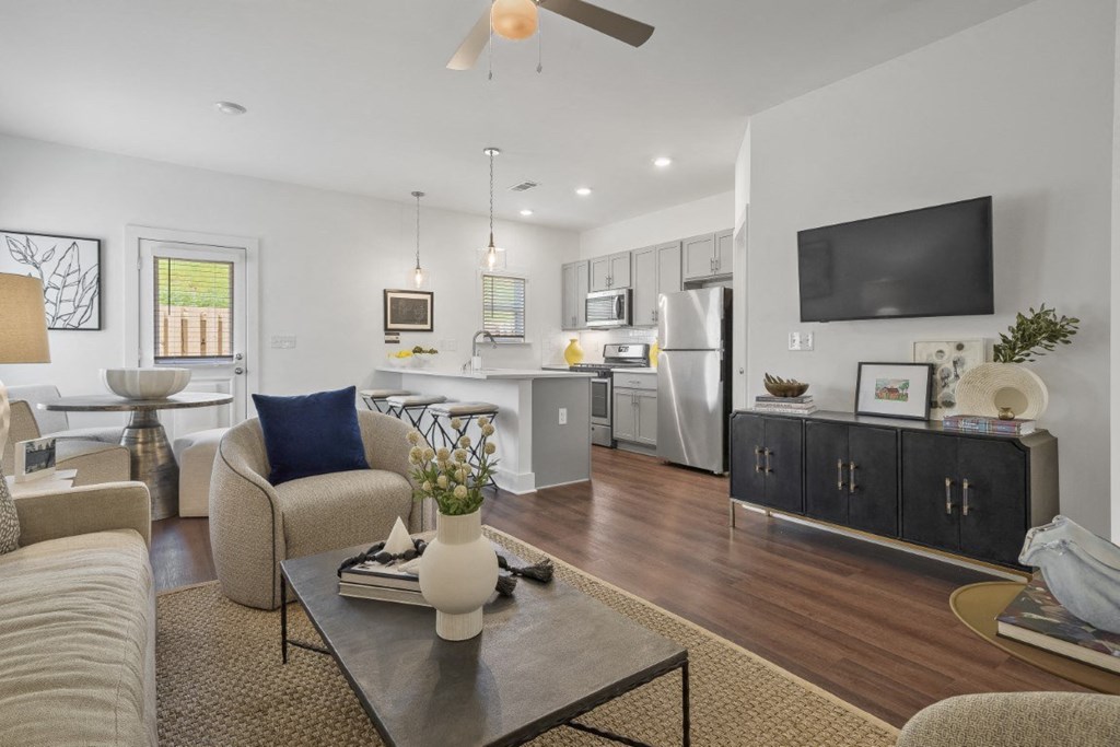 A modern living room with wood-style flooring, ceiling fan, bright light, and open floor plan.