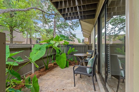 A patio with a table and chairs is surrounded by green plants.