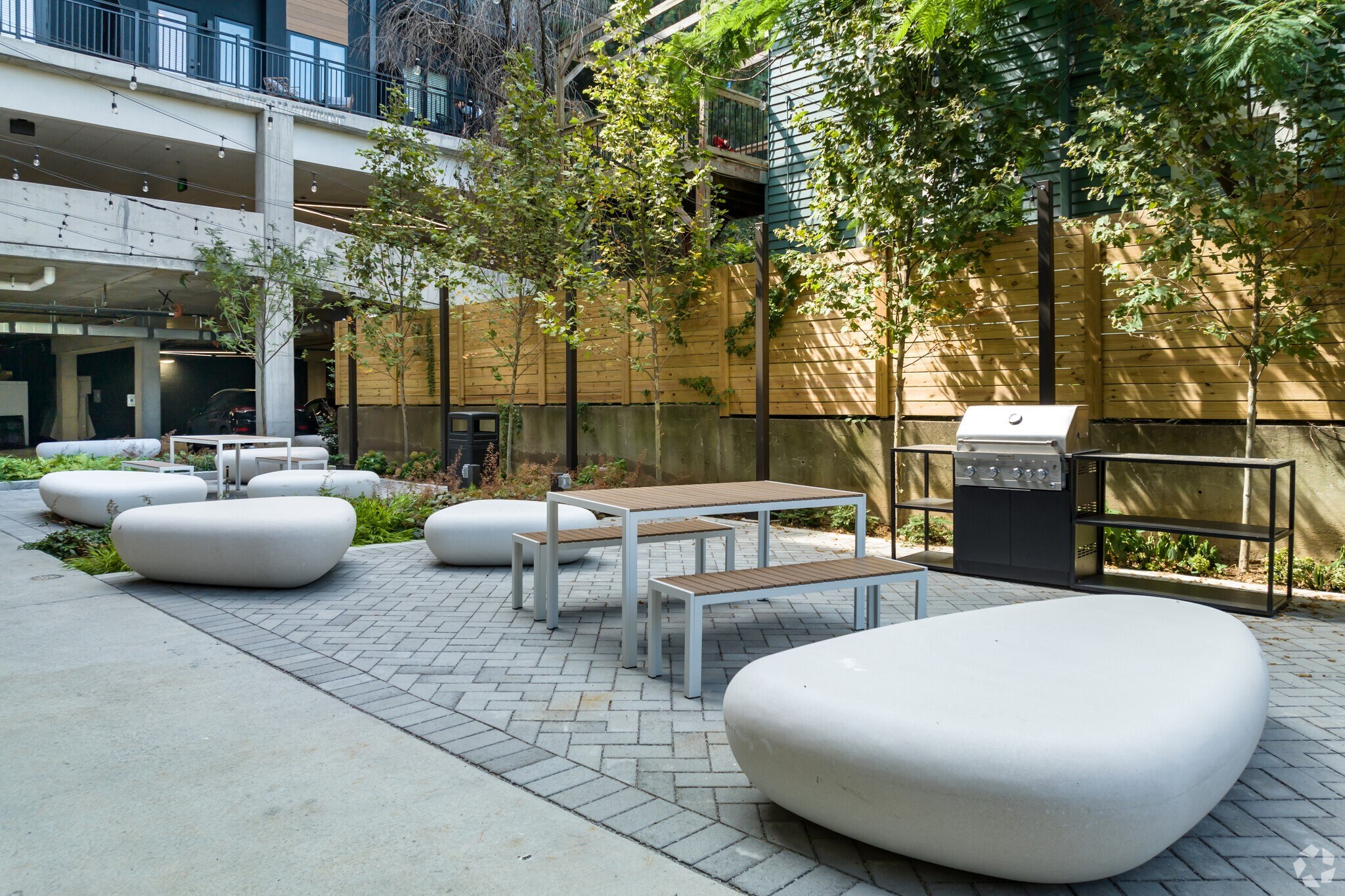 2 BR Apartments In Nulu, KY - Martin On Main - Courtyard With A Grill Surrounded By Greenery With Tables, Chairs, And Large Rocks For Seating