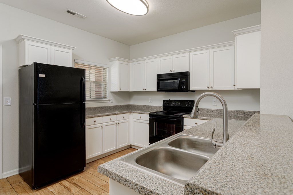 A black refrigerator is in a kitchen with white cabinets and a granite countertop.