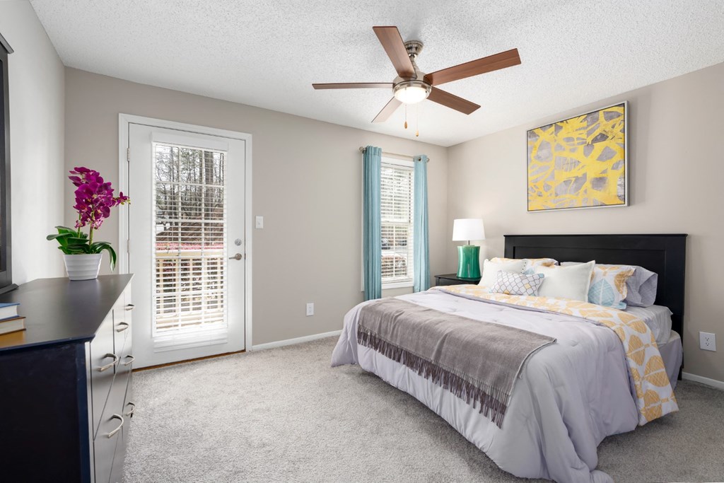 A bedroom with patio access, carpet flooring, ceiling fan, and a window at Summerchase at Riverchase in Hoover, Alabama.