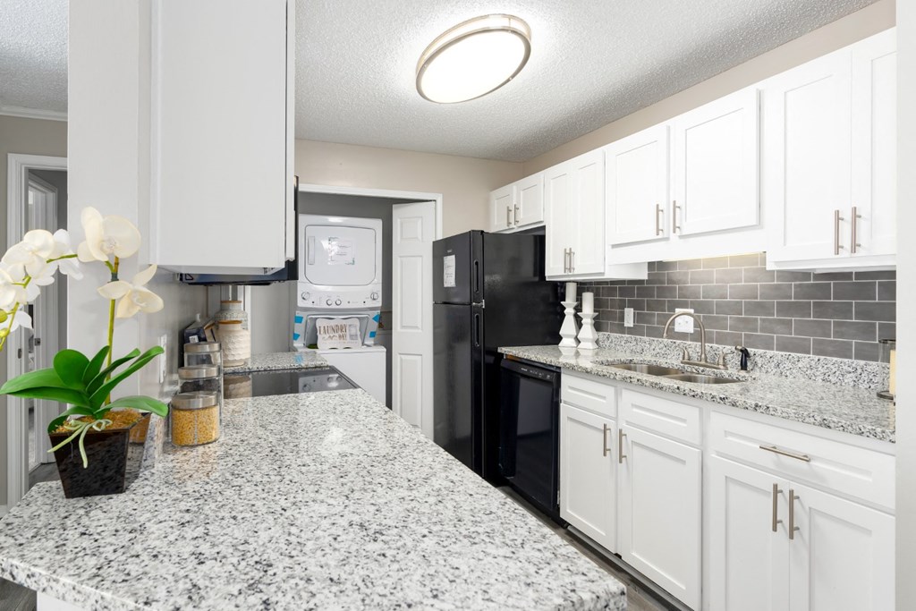 A kitchen with granite countertops, white cabinets, and a stackable washer and dryer at Summerchase at Riverchase in Hoover, Alabama.