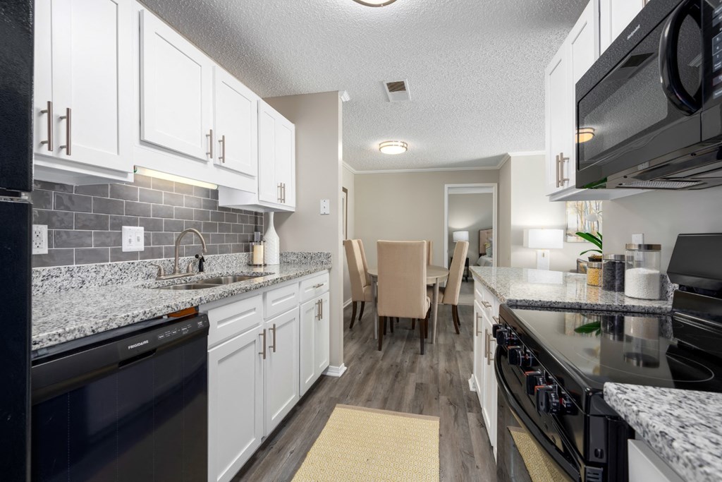 A kitchen with black appliances, granite countertops, white cabinets, and tile backsplash at Summerchase at Riverchase in Hoover, Alabama.