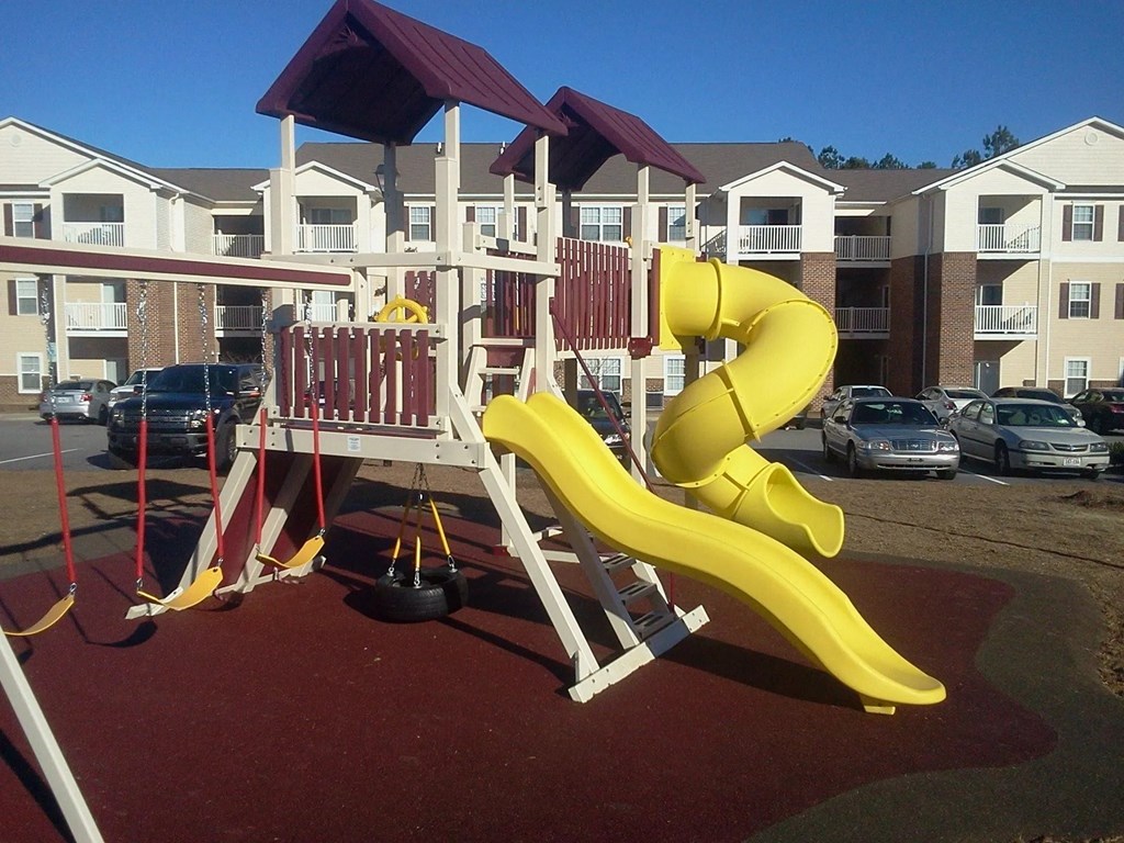 A yellow slide in a playground with a red roof.