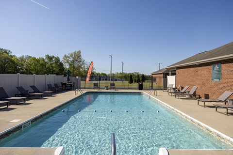A large outdoor swimming pool surrounded by lounge chairs and a fence.