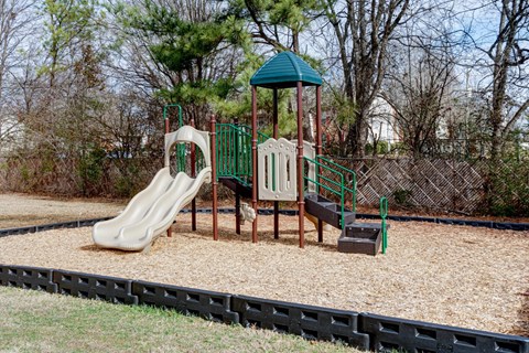 Playground with slides. A playground with a green roof, a slide, a wooden swing set, and a sandbox.