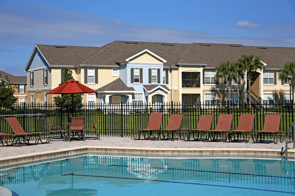 a swimming pool with chairs in front of an apartment building